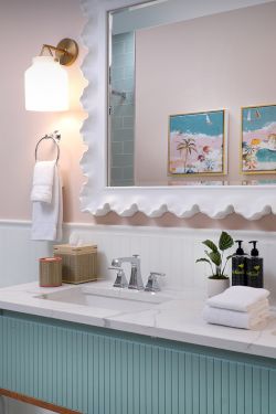 A bright modern bathroom with a glass shower, white vanity and sink, wall art, and towels on the counter.
