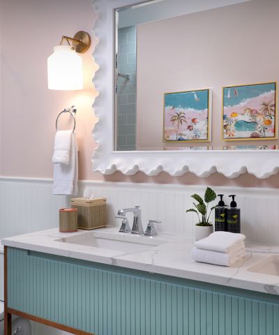 A bright modern bathroom with a glass shower, white vanity and sink, wall art, and towels on the counter.