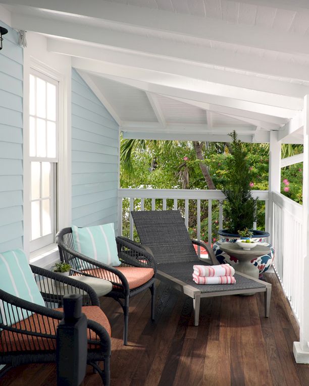 A bright porch with wicker chairs, striped cushions, and a tray of snacks overlooking lush tropical greenery and flowers, in daylight.