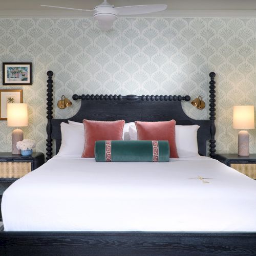 A stylish hotel bedroom with a black canopy bed, patterned wallpaper, lamps, and framed art in soft light.