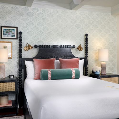A stylish bedroom with a dark four-poster bed, patterned wallpaper, and lamps on matching nightstands.