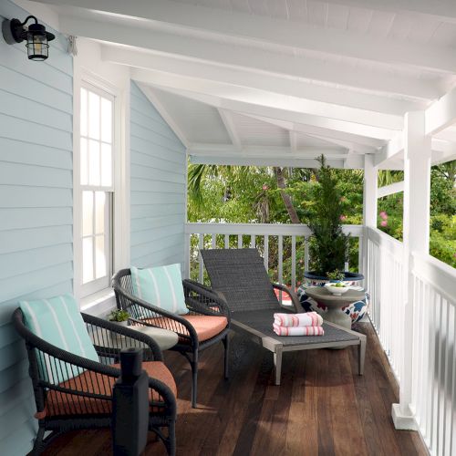 A sunny porch with wicker chairs and a small patio table, overlooking lush tropical greenery and colorful flowers outside.
