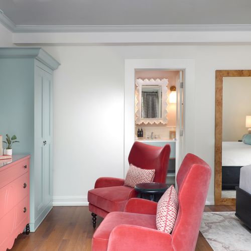 Bright room with a blue dresser, red armchairs, a side table, and large framed mirrors reflecting a bathroom vanity.