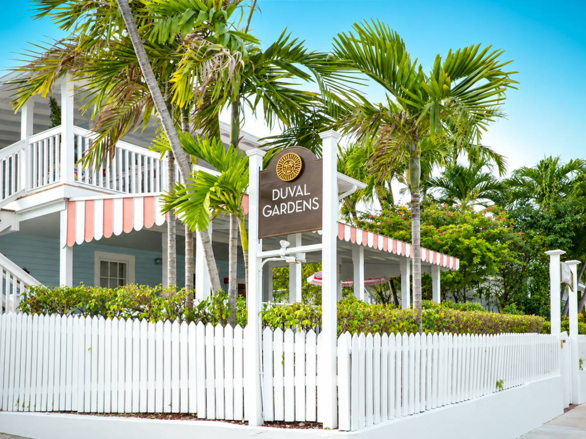 Tropical resort grounds with palm trees and a &ldquo;Duval Gardens&rdquo; sign beside a white building.