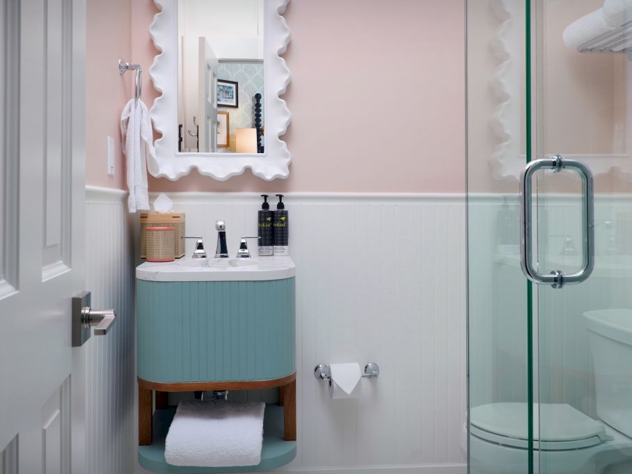 A bright bathroom with a blue vanity, framed mirror, towels, soap bottles, and a glass shower door.