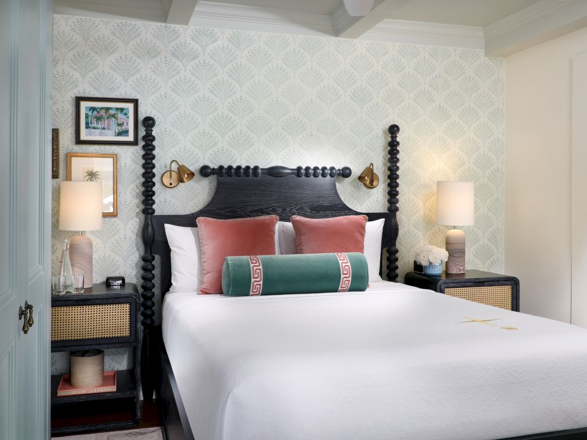 A stylish bedroom featuring a four-poster bed, patterned wallpaper, framed art, lamps, and neatly arranged pillows.