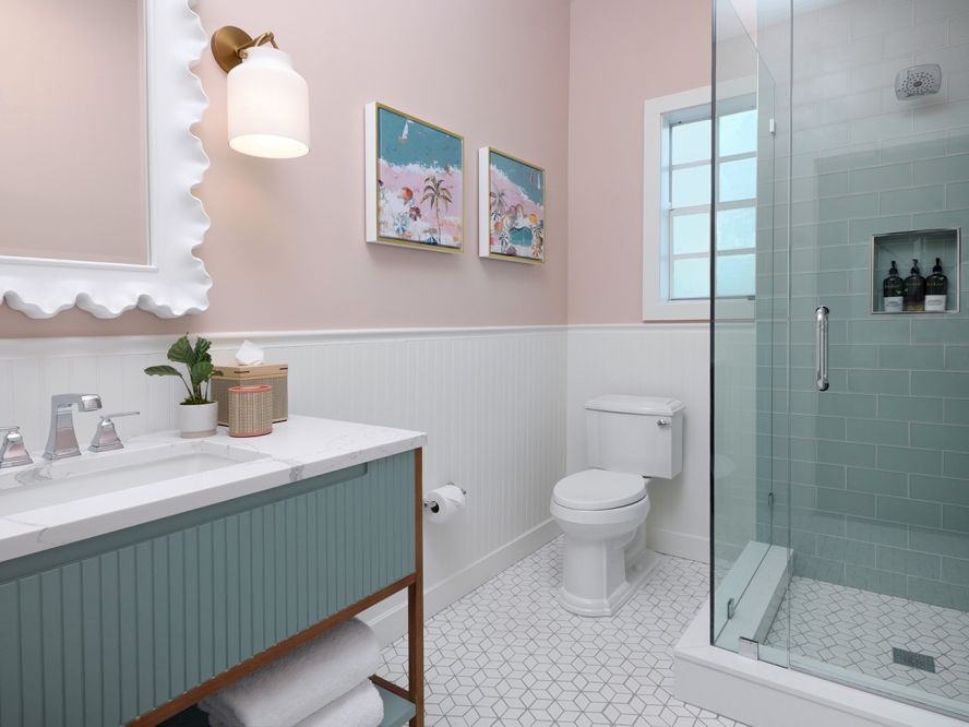 A bright modern bathroom with a vanity, toilet, framed art, and a glass shower with teal tile walls.