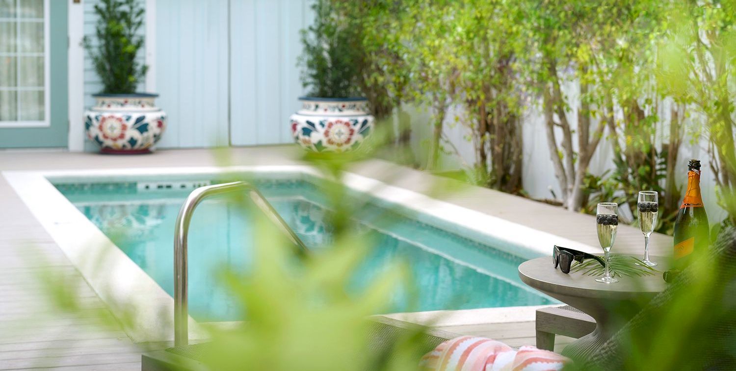 Outdoor poolside patio: turquoise pool, lounge chair, and a small table with champagne bottle and glasses.