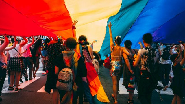 A lively crowd dances under bright red and blue festival tents, with people holding up their hands and celebrating together.